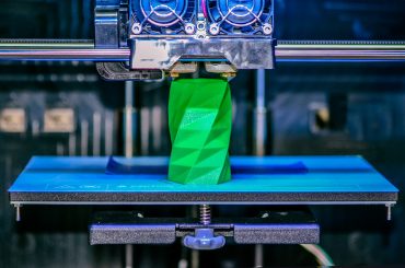3D printer works and creates an object from the hot molten plastic close-up. Automatic three dimensional 3d printer performs plastic green colors modeling in laboratory.