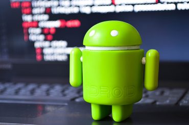 A green android figure stands on a laptop on a programming code screen. View through a magnifying glass. July 2020. Kiev, Ukraine